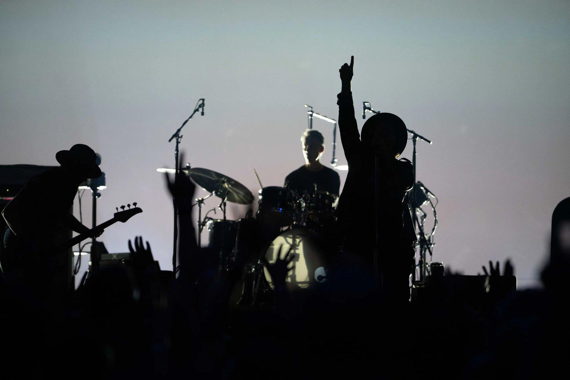 Band silhouetted against a pale backdrop, the singer's arm raised with one finger to the sky