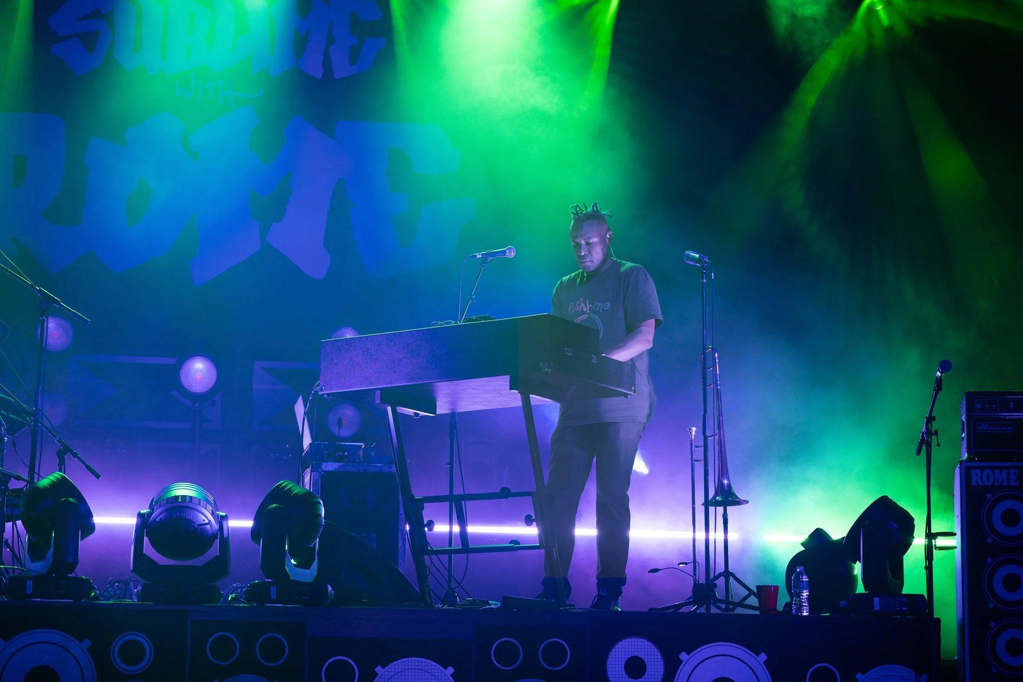 Keyboardist playing through green and violet fog in front of a graffiti backdrop
