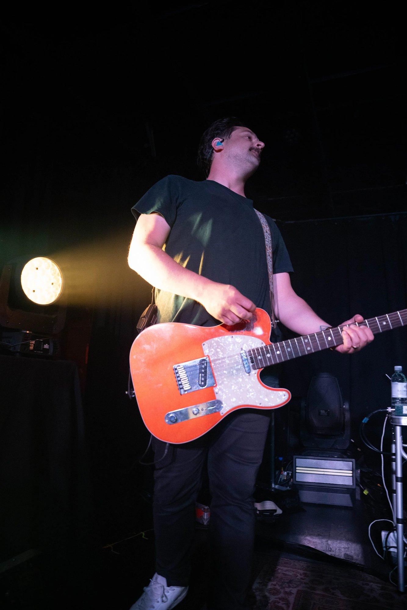 Guitarist with an orange Telecaster looking over his shoulder in a single amber spot