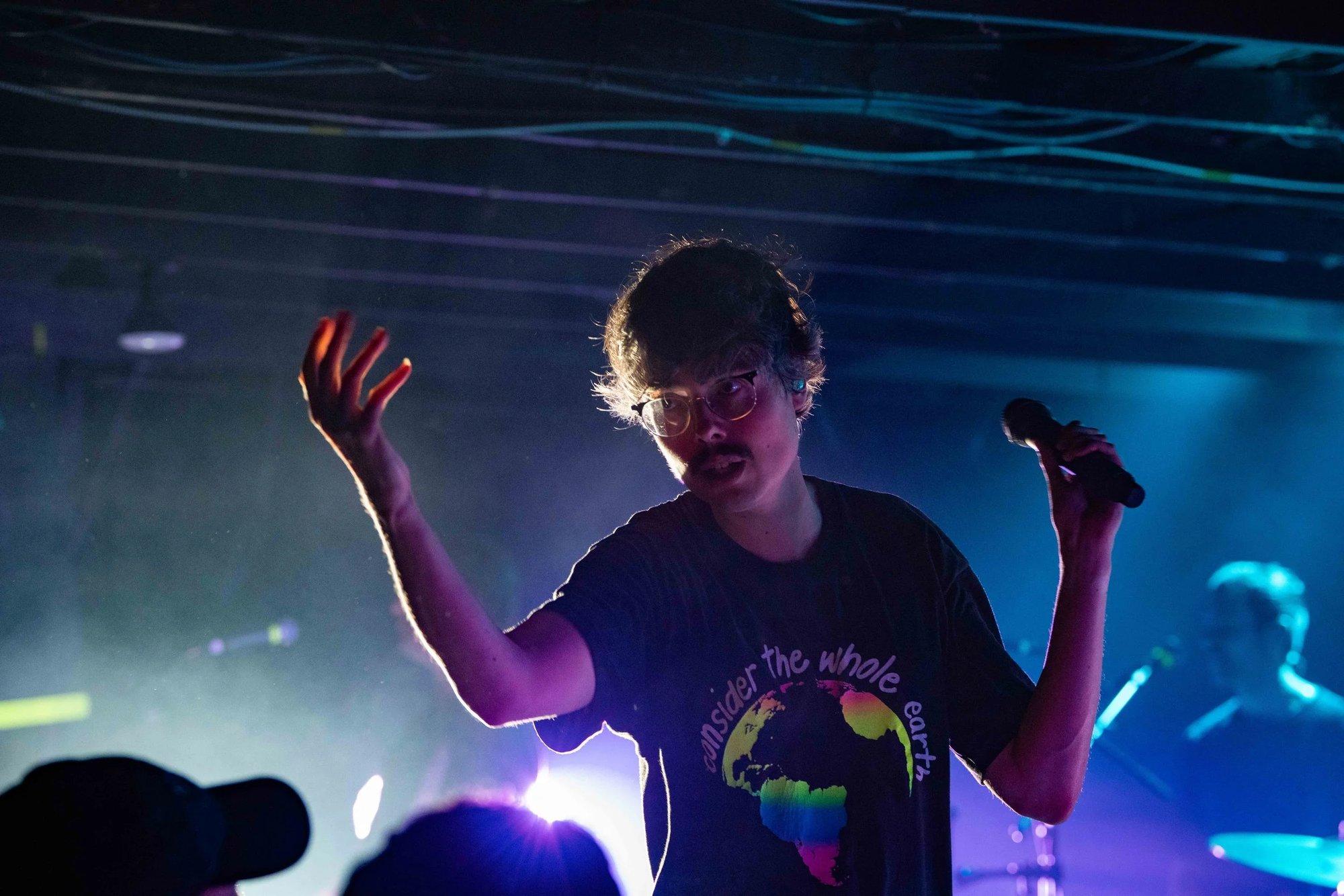 Singer gesturing mid-verse, rim-lit in teal haze with a starburst flare behind
